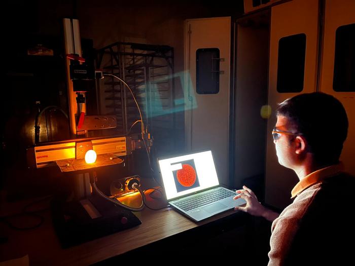 A man sits at a table with a laptop computer while a bright light shines on an egg