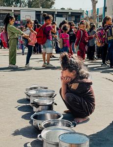 A child crouches next to pots and pans at a UNRWA school in Gaza, 2025 (credit UNRWA)