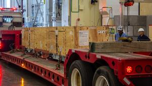 A flatbed truck brings the magnet bundle, still in its crate, within a large space adjacent to NSTX-U known as the Fusion Research and Technology Hub.