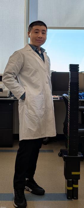 Dr. Xuyu Qian in his current laboratory, standing beside a collection of external hard drives containing raw spatial transcriptomics data from his groundbreaking human brain development research.
