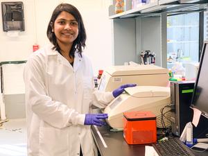 A woman in a lab coat and gloves standing next to lab equipment
