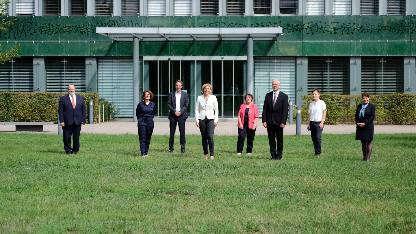 Eight People In Business Clothes On Some Grass In Front Of A Building