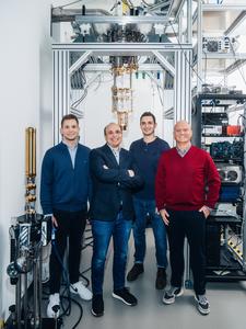 From right to left, Rostyslav Serha, Andrii Chumak, David Schmoll and Sebastian Knauer are standing in front of a cryostat. This device is used to generate and stabilise extremely low temperatures.