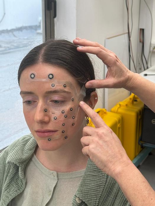 Illustration of a participant in the study with an EMG electrode measuring her facial expressions activation.