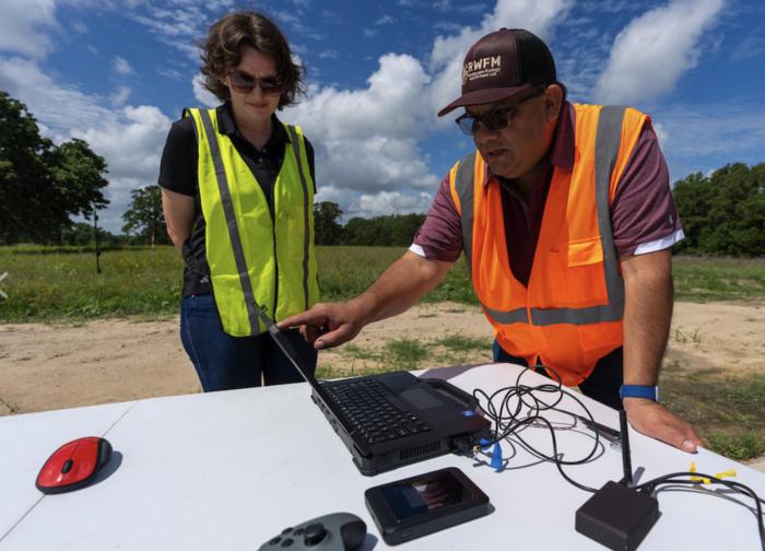 Humberto Perotto and a student view information on a laptop that is set up in the field.