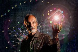 A man with glasses stands in front of a digital network diagram, holding up his hand with a glowing network sphere above his palm.