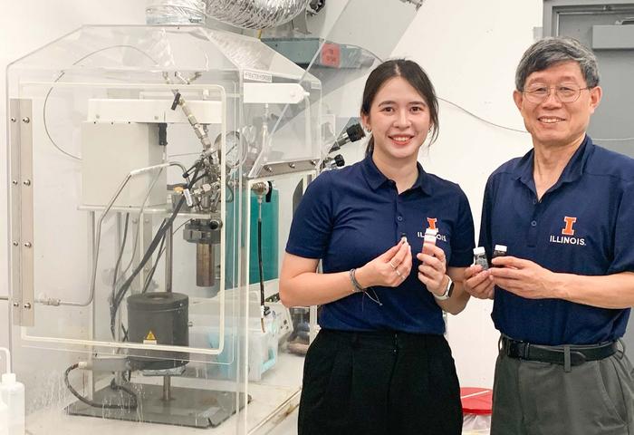 A man and a woman wearing blue t-shirts with University of Illinois logos hold vials in their hands, standing next to laboratory equipment.