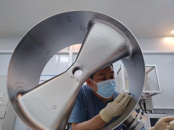 The employee is  conducting inspections for defects of the superconducting cavity.