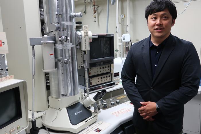 Sugimoto speaks about his research in front of the electron microscope installed at his laboratory.