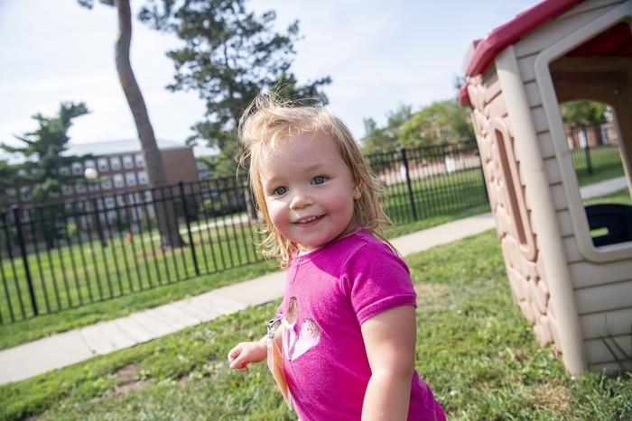 Toddler standing outside by a play structure on a lawn