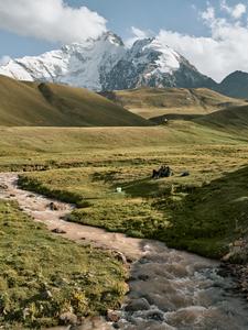 A stream with mountain glaciers and snow that supply it in the background