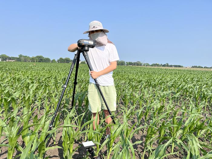 A man standing with a camera on a tripod in a maize field