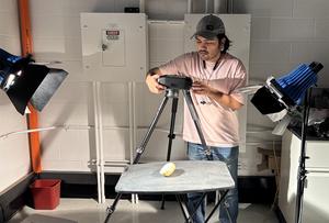A man in a lab setting holding a camera over a sweet potato on a table