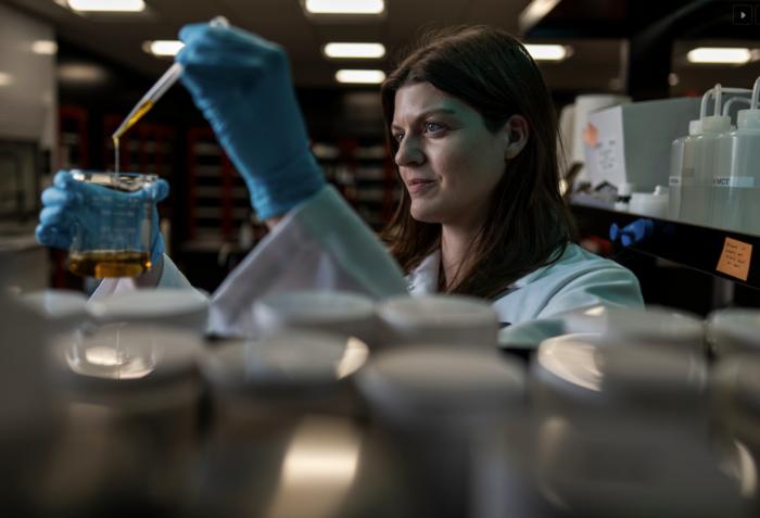 Lauren Muhlberger wearing blue gloves and adding liquid to a beaker using a dropper