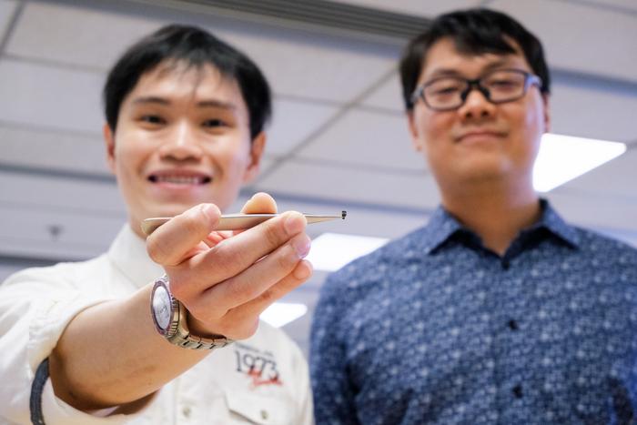 NTU Assoc Prof Lum Guo Zhan (right) and PhD student Nicholas Yong Wei Foo (left), who is holding the seed-sized 5-in-1 surgical robot with a pair of tweezers.