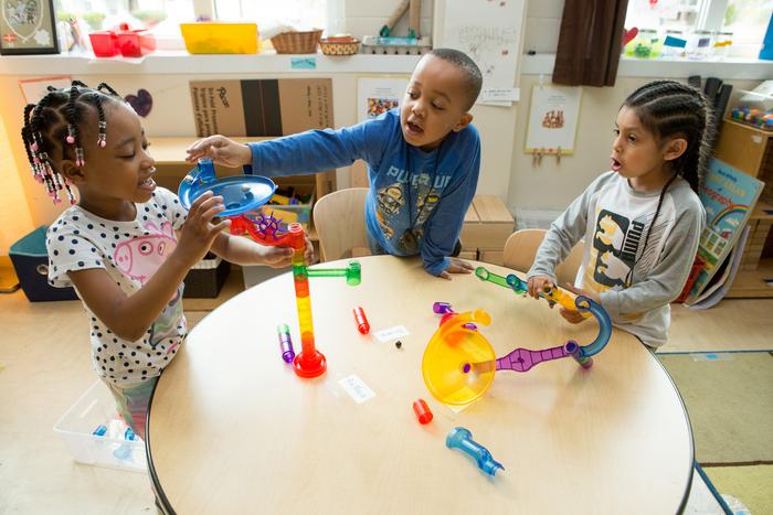 Three kindergartners play with marbles