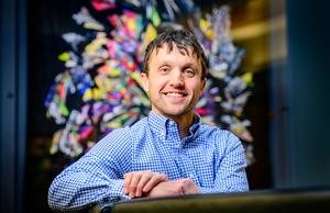 A man in a blue shirt in front of a colorful, abstract background