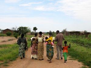 A group of women, children and one male are walking with their backs to the camera in a rural setting in Tanzania.